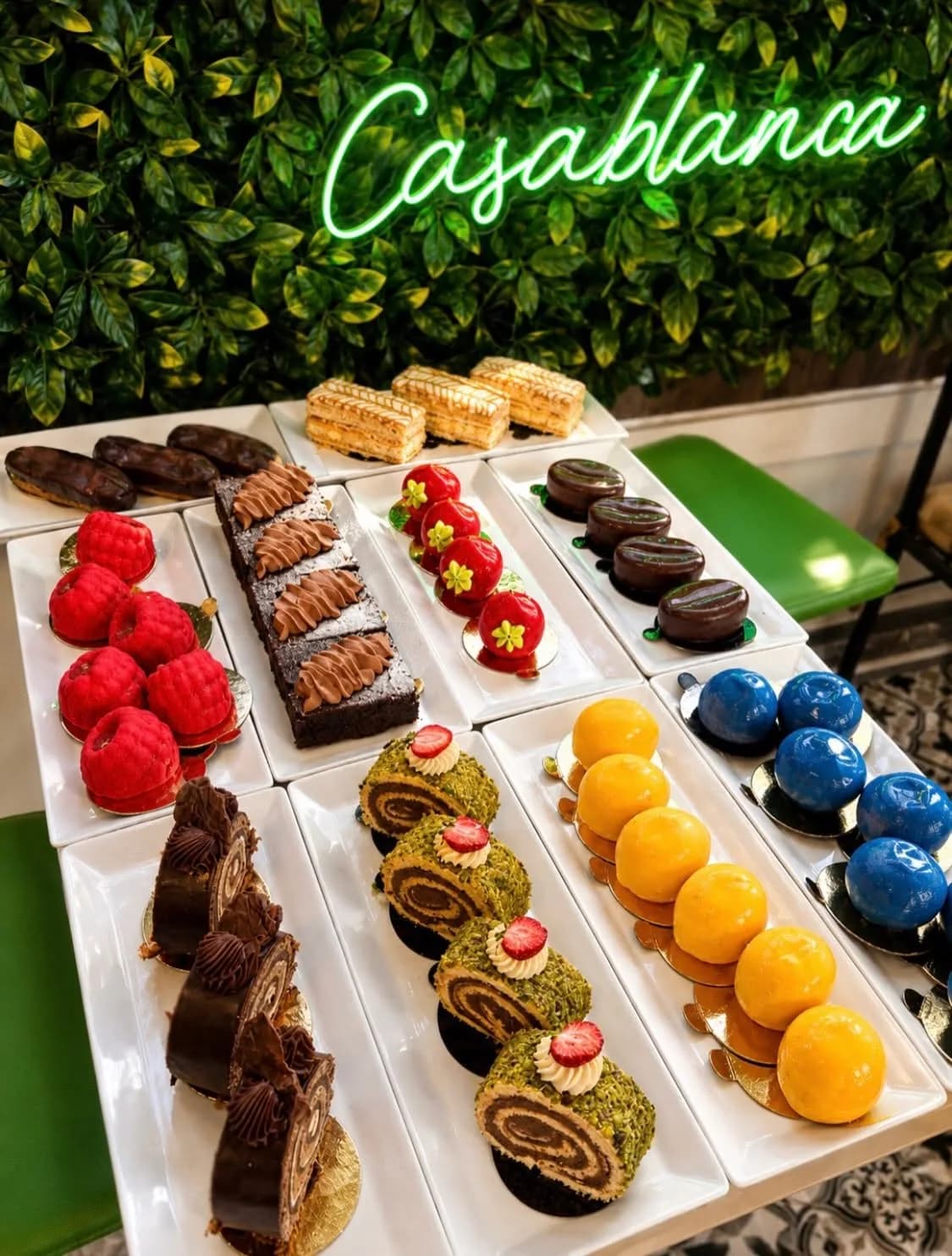 Trays of éclairs, mille-feuille, brownies, pistachio rolls and colourful mousse cakes beneath Casablanca’s green neon sign